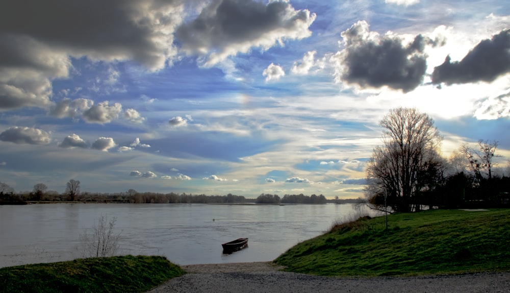 body of water near green grass field under cloudy sky during daytime