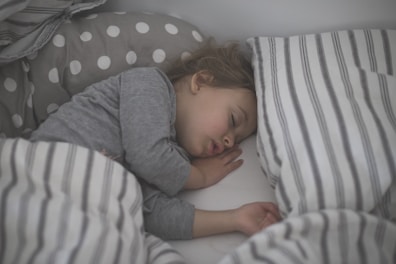 baby in gray long sleeve shirt lying on white and black stripe bed