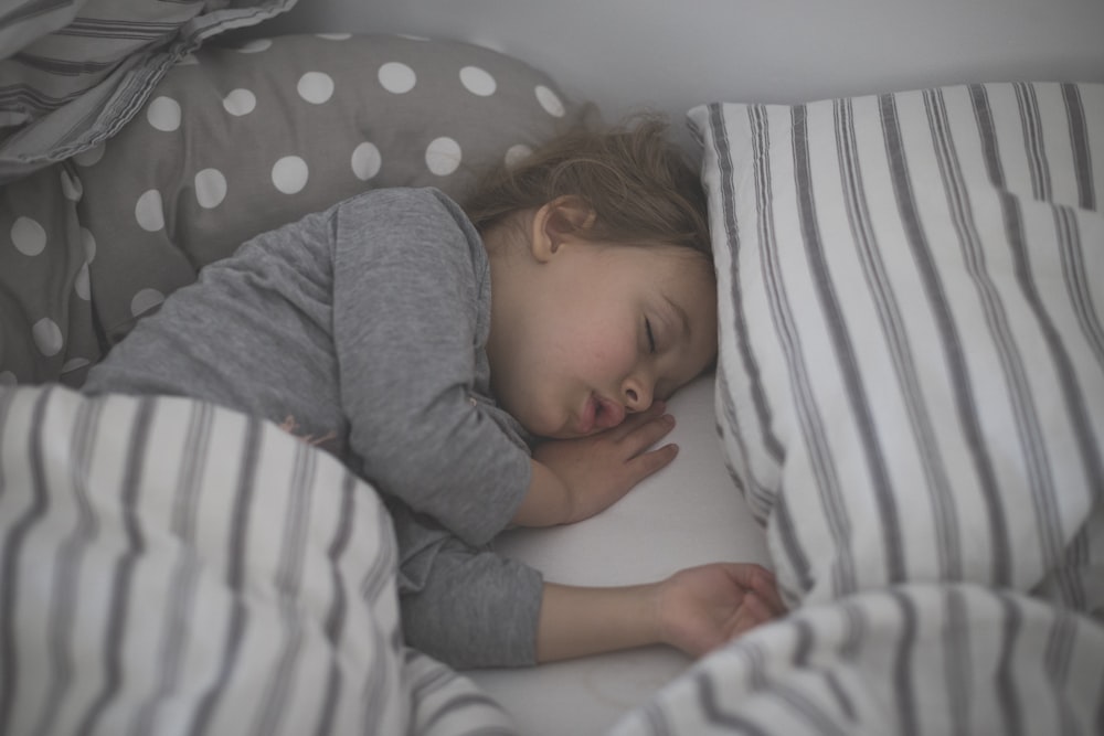 baby in gray long sleeve shirt lying on white and black stripe bed