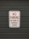 A white sign with red text that reads 'No Parking in Front of Garage Door' is mounted on a dark gray garage door.