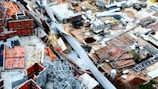 A densely stacked construction site filled with various materials such as metal beams, wooden planks, and concrete blocks. The area is cluttered with a mix of construction equipment and supplies, indicating active or ongoing building activity. The scene is characterized by a chaotic yet industrious atmosphere, typical of large-scale construction projects.