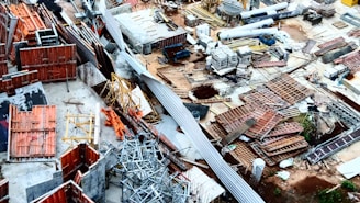 A densely stacked construction site filled with various materials such as metal beams, wooden planks, and concrete blocks. The area is cluttered with a mix of construction equipment and supplies, indicating active or ongoing building activity. The scene is characterized by a chaotic yet industrious atmosphere, typical of large-scale construction projects.