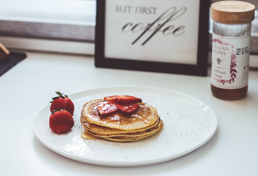 a white plate topped with pancakes covered in syrup and strawberries