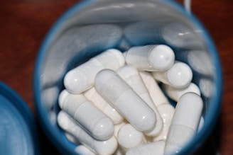 A container filled with white capsules viewed from above, set against a dark background. The capsules are tightly packed inside the container, reflecting light off their surfaces.