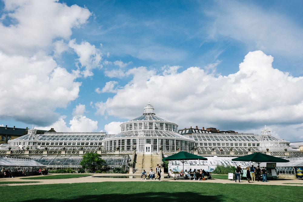 people walking on green grass field near white building under blue and white cloudy sky during