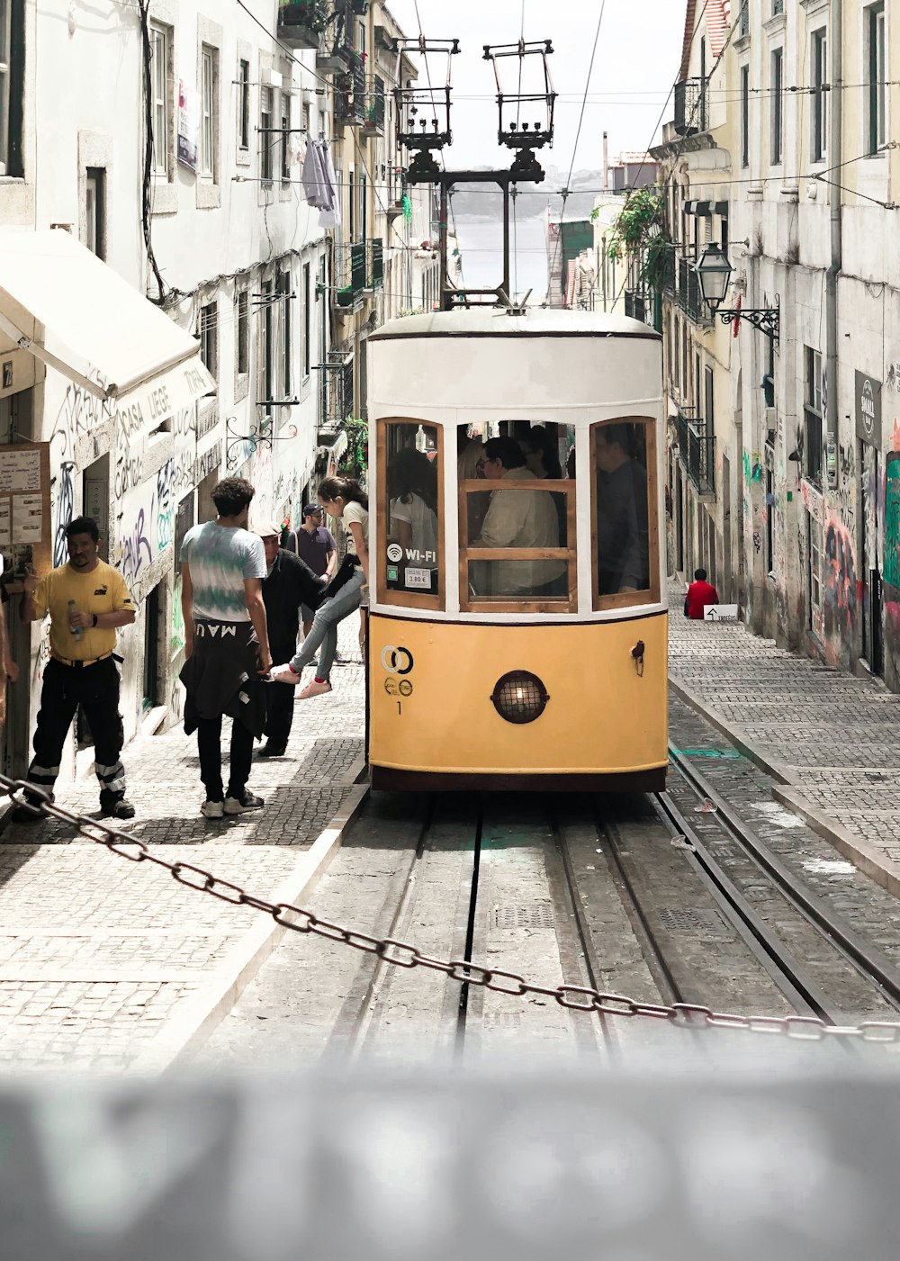 people walking on sidewalk near yellow tram during daytime