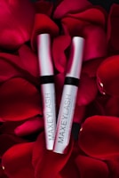 Two silver tubes labeled 'MAXEYLASH eyelash enhancing serum' are nestled amongst vibrant red rose petals.