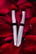 Two silver tubes labeled 'MAXEYLASH eyelash enhancing serum' are nestled amongst vibrant red rose petals.