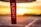 A red tag with white text reading 'FLIGHT', hanging prominently in the foreground with a blurred background of a warm, glowing sunset. The horizon line and abstract shapes suggest an airport setting.