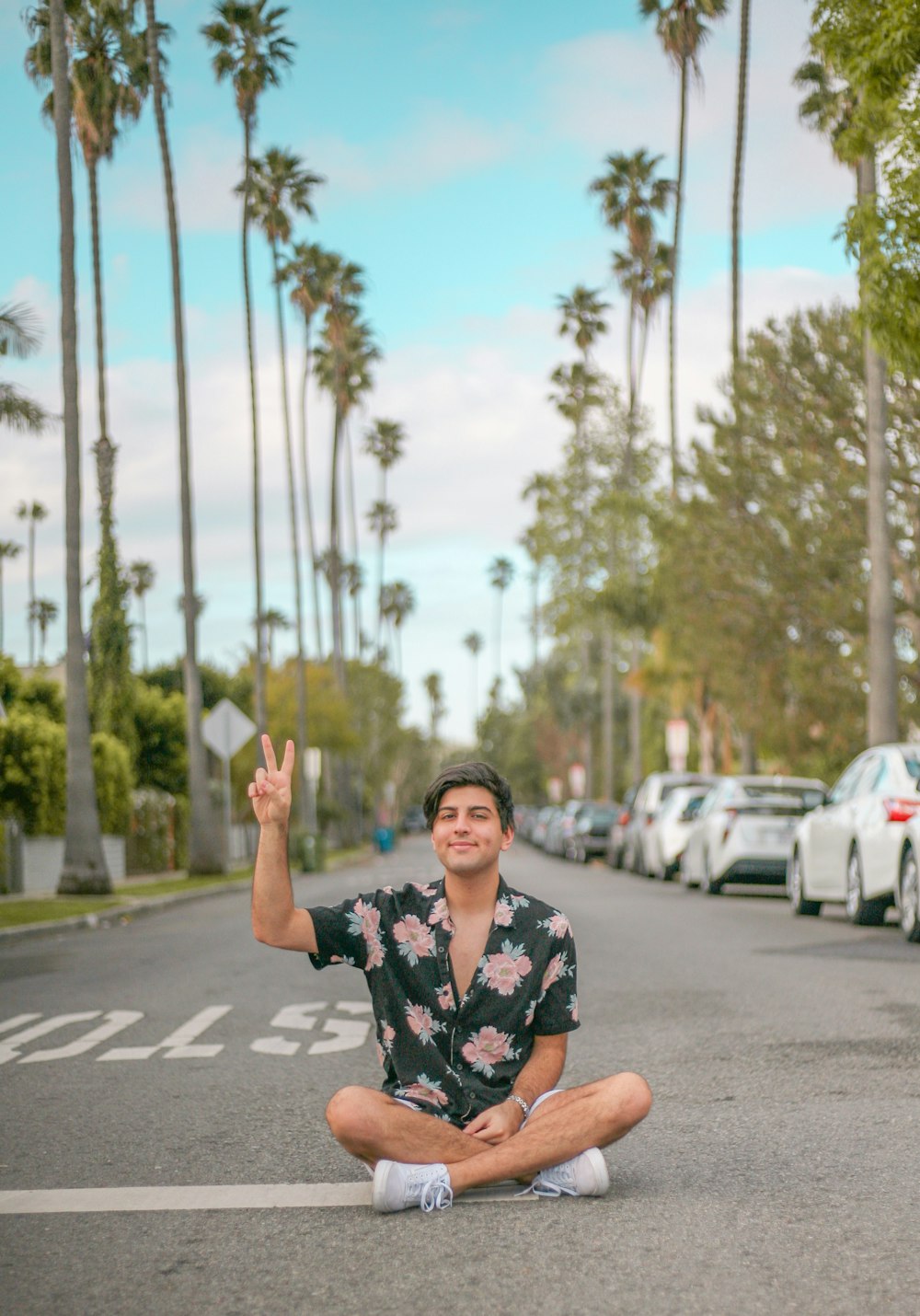 man in black and white floral button up t-shirt sitting on road during daytime