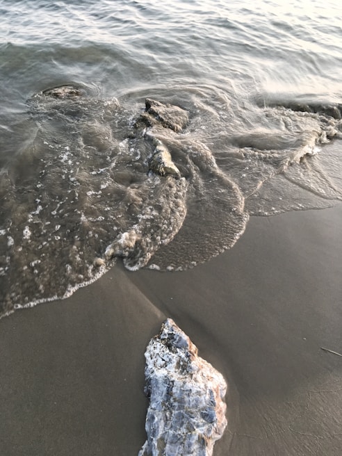 A gentle wave washing over smooth sea glass fragments on a rocky shore