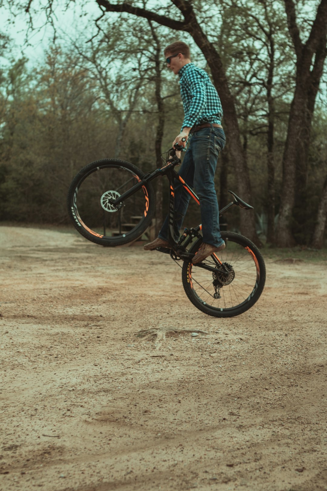 man in blue and white checkered dress shirt riding black bicycle on brown dirt road during