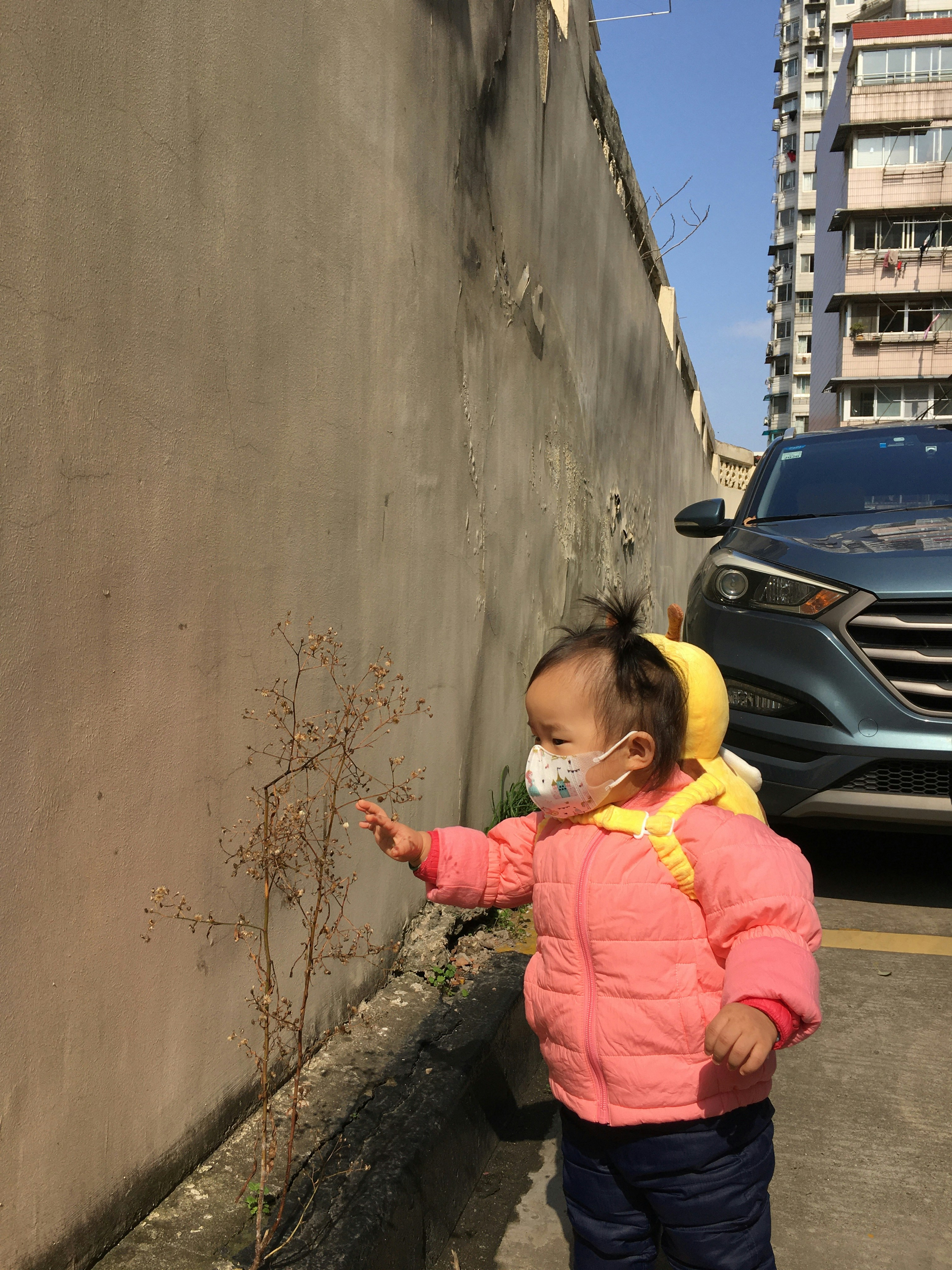 girl in pink jacket and yellow helmet standing beside gray car during daytime