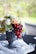 A decorative arrangement featuring a mix of flowers and clusters of grapes in a classic black urn. White, peach, and green flowers are complemented by red and green grapes cascading over the edge. The setting is on a black tablecloth, enhanced by a sheer white fabric draped gracefully around the base of the urn.
