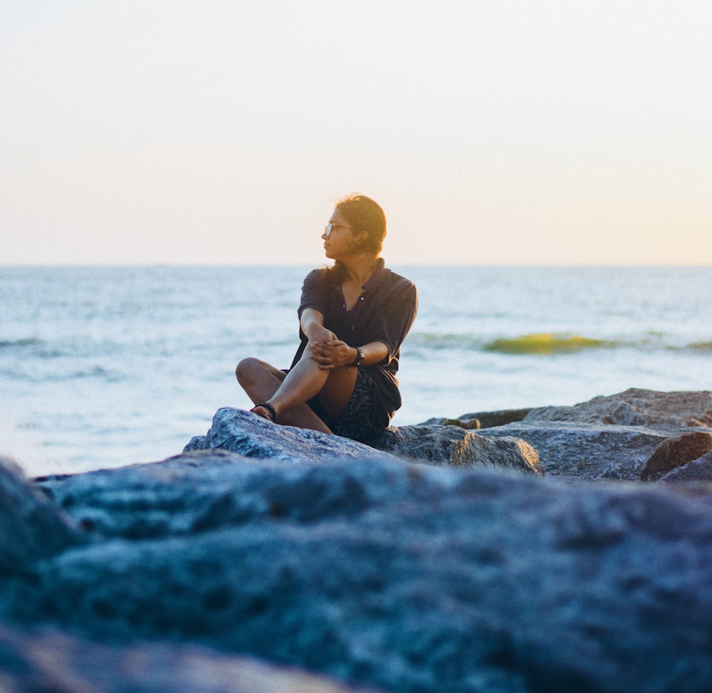 woman in black tank top sitting on rock near sea during daytime