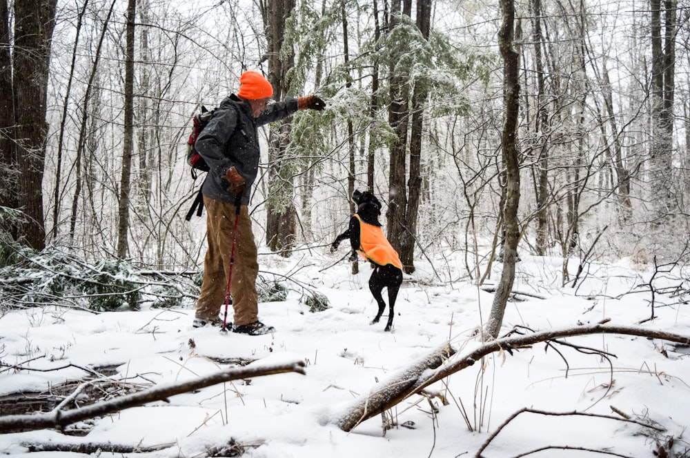 person in orange jacket and black pants standing on snow covered ground surrounded by bare trees