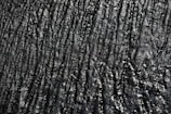 A textured surface with irregular, wavy lines and a glossy appearance. The surface has a dark, almost black color with reflective highlights that give it a slick, shiny look.