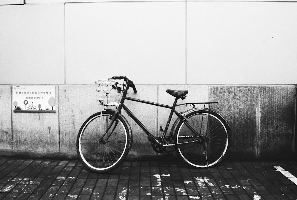 grayscale photo of city bicycle leaning on wall