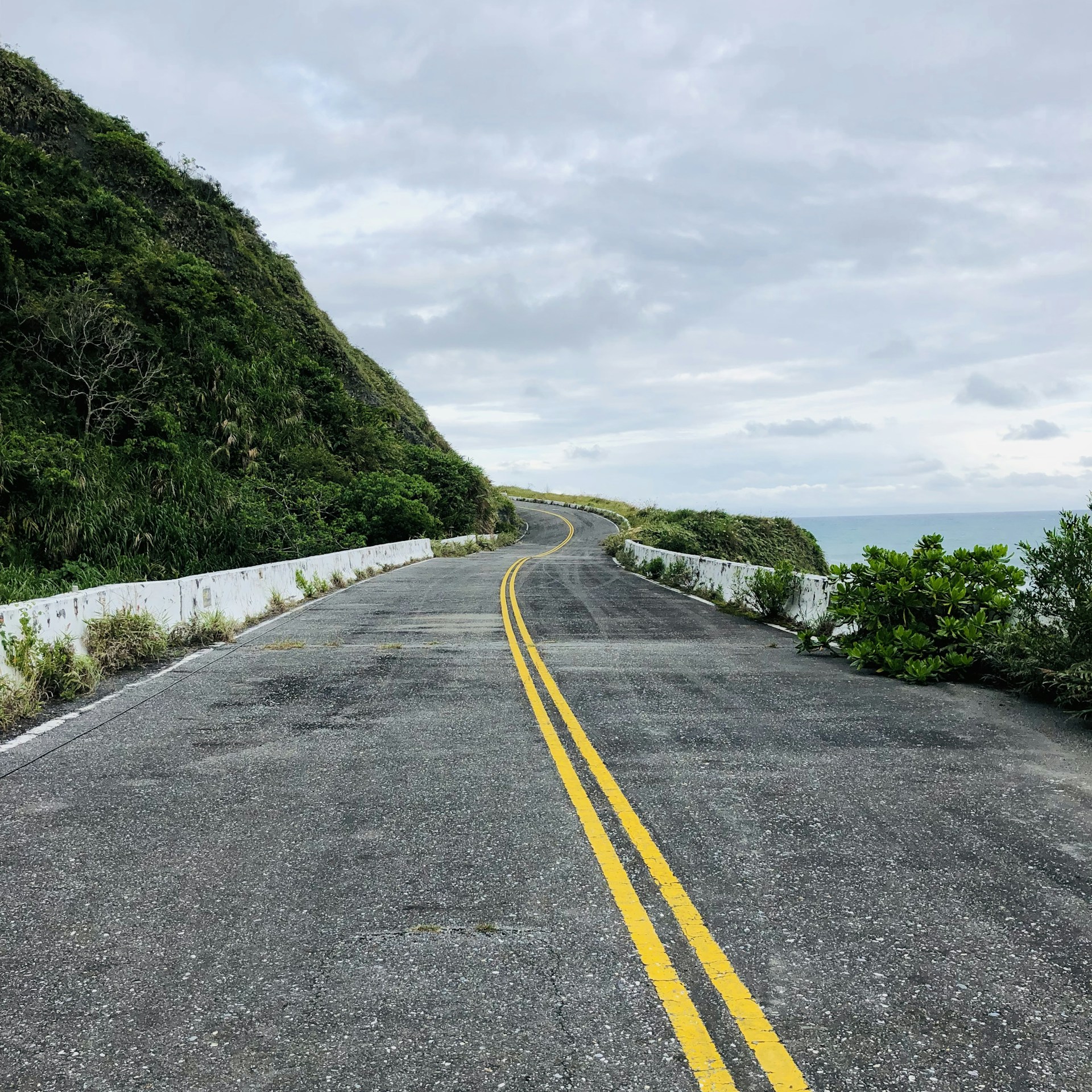 gray concrete road between green grass field under white cloudy sky during daytime