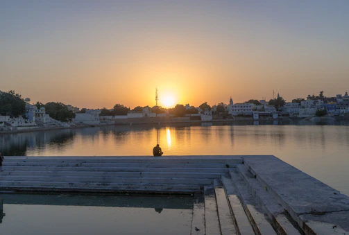 A calm outdoor scene with a person reflecting near a lake at sunset.