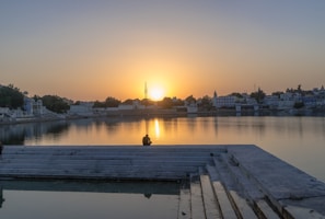 A peaceful scene of a person meditating by a calm lake at sunset.