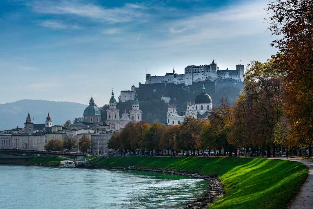white and brown concrete building near green grass field and body of water under blue sky, Castle of Salzburg