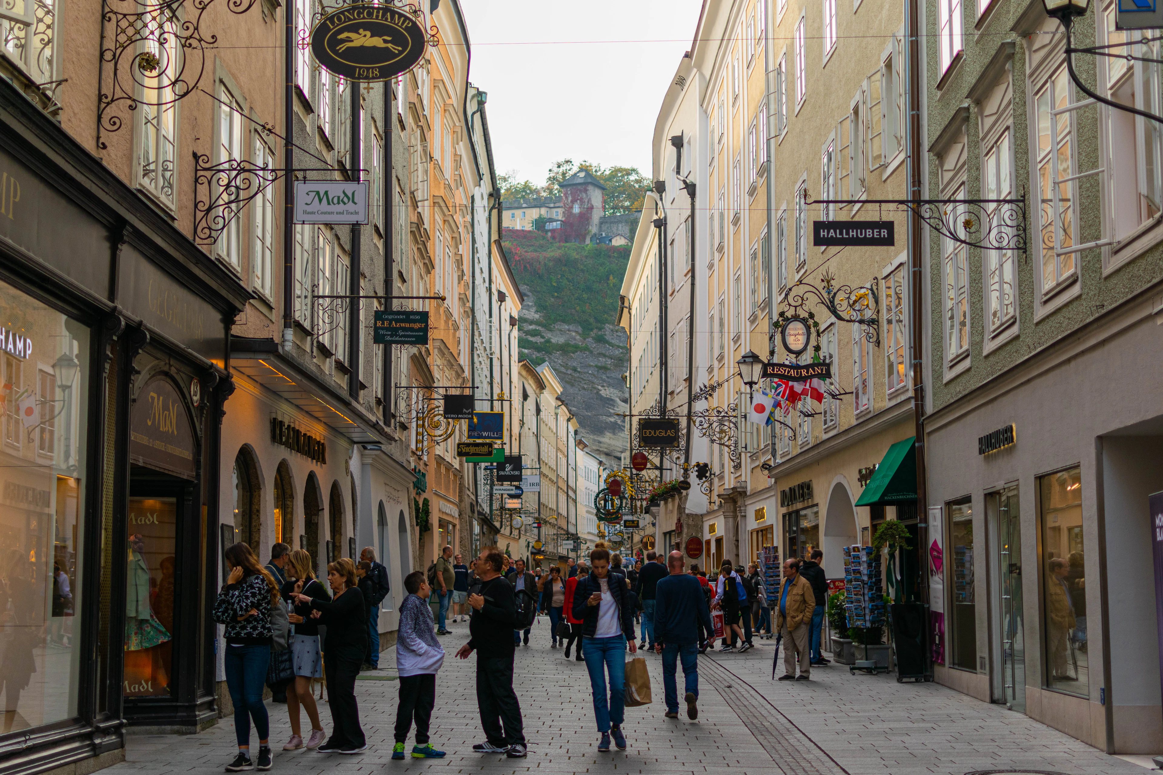 Shoppers filling the narrow Getreidegasse in Salzburg beneath its wrought-iron guild signs, the fortress hill at the end