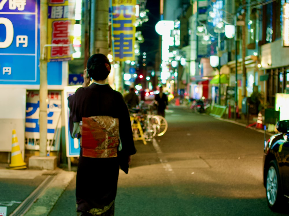 man in black and white floral shirt standing on sidewalk during night time