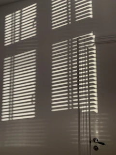 Abstract shadows cast by window blinds creating geometric shapes on a white wall.