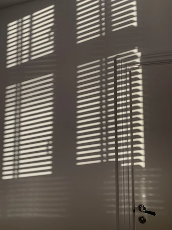Abstract shadows cast by window blinds creating geometric shapes on a white wall.