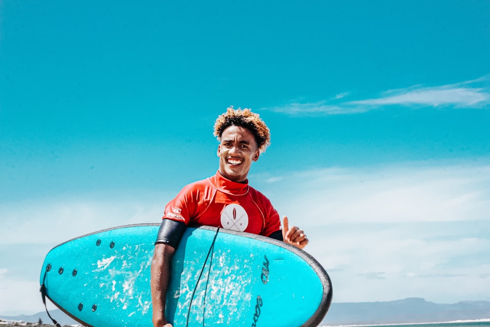 man in red and blue crew neck t-shirt holding blue surfboard