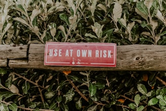 A red warning sign with white letters, reading 'USE AT OWN RISK', is attached to an aged wooden log. The background consists of dense green foliage.