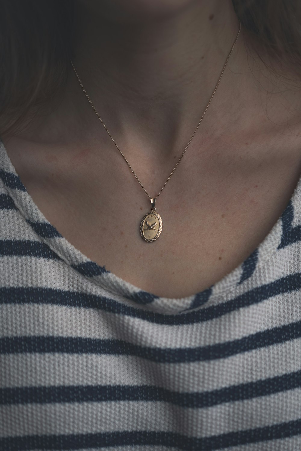 woman in white and gray striped shirt wearing gold heart pendant necklace