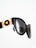 A close-up of stylish black sunglasses with gold detailing, featuring a decorative emblem. The design has a glossy finish and the lenses are tinted dark.