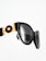 A close-up of stylish black sunglasses with gold detailing, featuring a decorative emblem. The design has a glossy finish and the lenses are tinted dark.