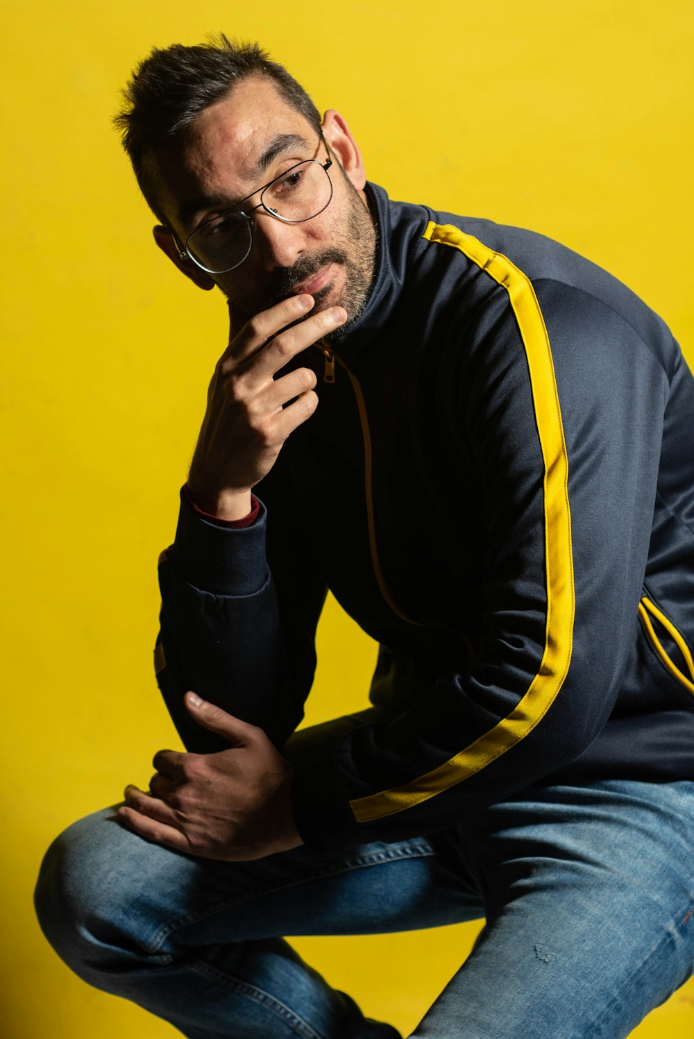 man in black and yellow hoodie and blue denim jeans sitting on chair