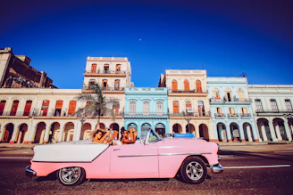 pink convertible car parked near beige concrete building during daytime