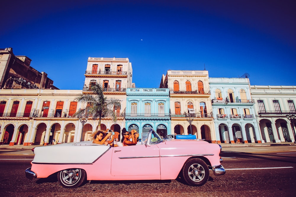 carro conversível rosa estacionado perto do edifício de concreto bege durante o dia