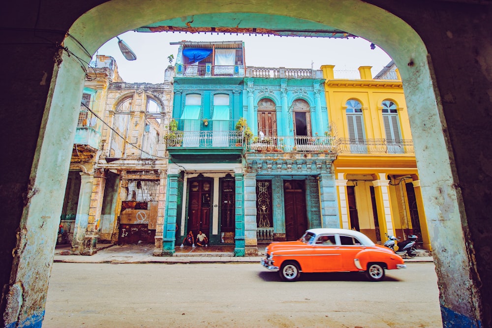 orange and white sedan parked beside brown concrete building during daytime