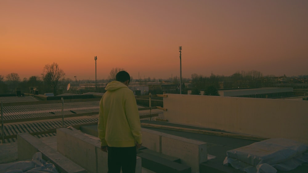 Mann in gelbem Kapuzenpulli steht bei Sonnenuntergang auf dem Dach des Gebäudes