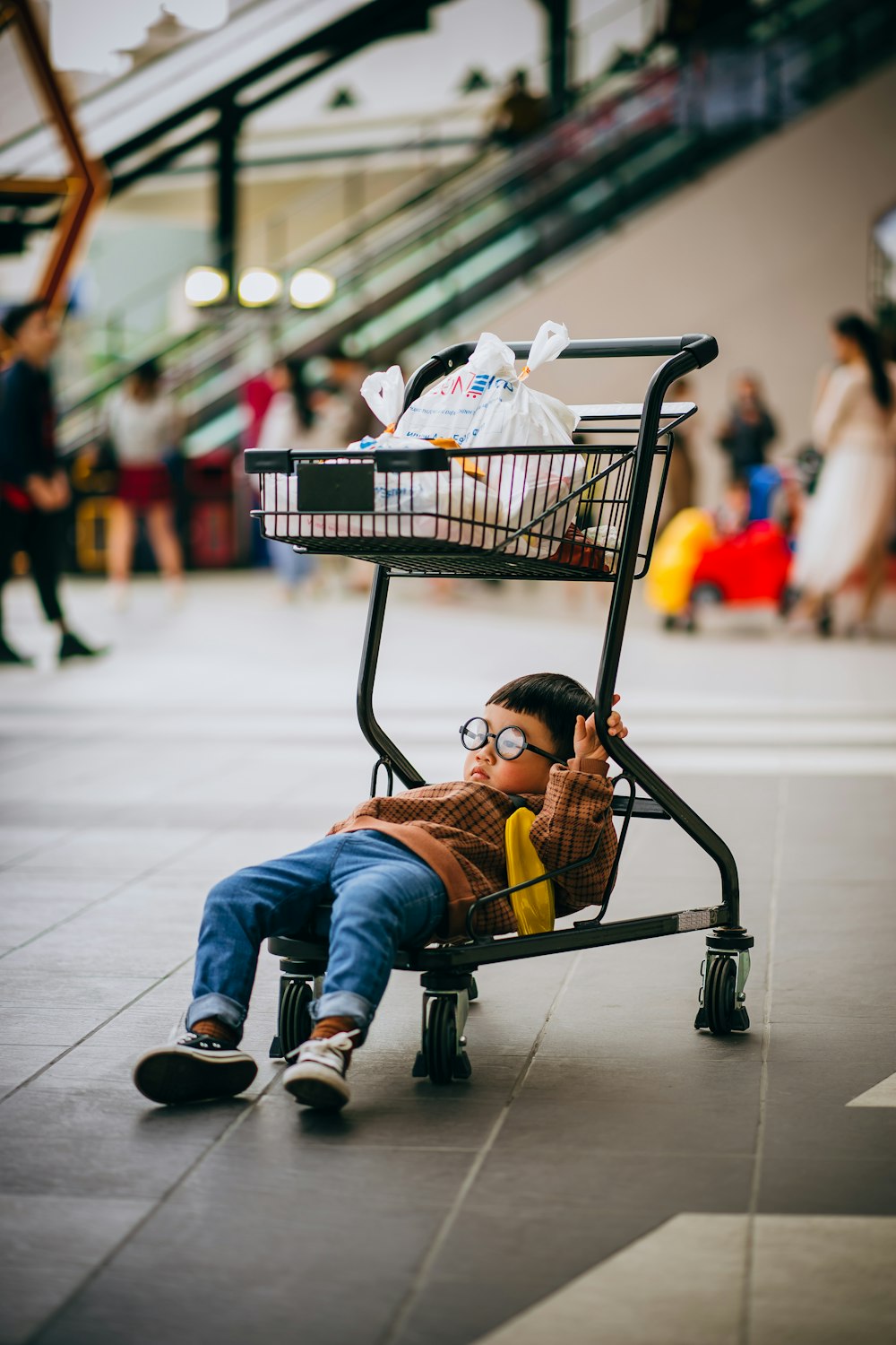 boy in orange jacket sitting on black shopping cart