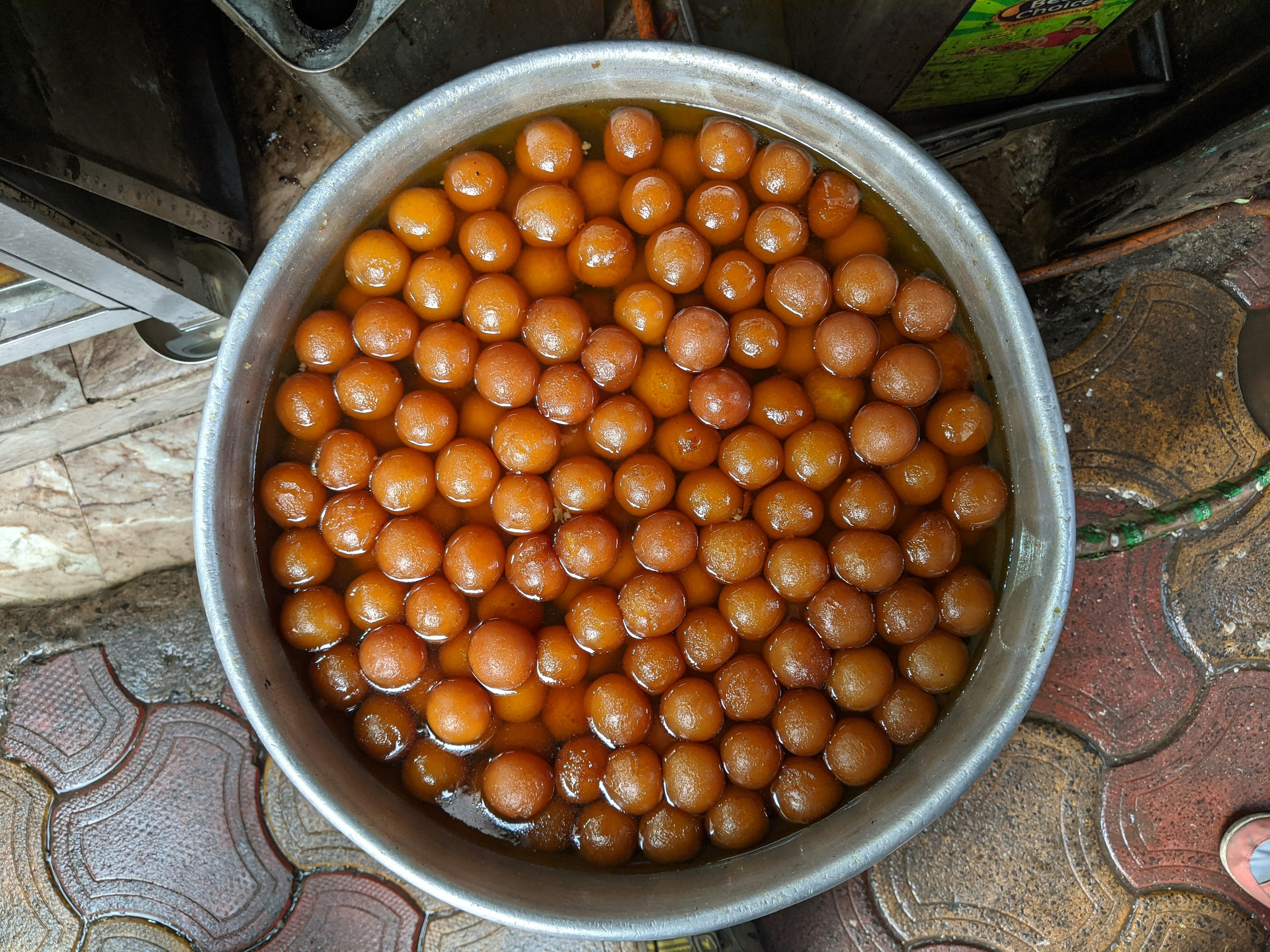 Close-up of freshly made Gulab Jamun spheres glistening in rose-saffron syrup in a dark copper bowl