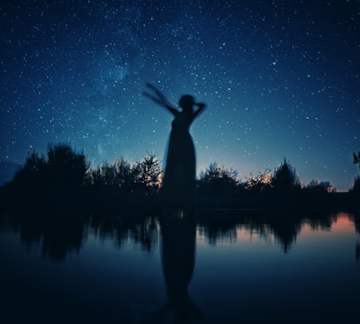 silhouette of woman standing on rock near body of water during night time