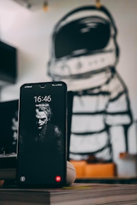 A smartphone displaying a monochrome wallpaper with a sinister-looking character. The phone's screen shows a time of 16:46 and a date of Saturday, February 29. The background features a mural of an astronaut in a stylized, black-and-white outline, which creates a contrast with the phone's display.