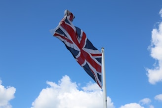 A Union Jack flag waves in the breeze against a bright blue sky with scattered white clouds.