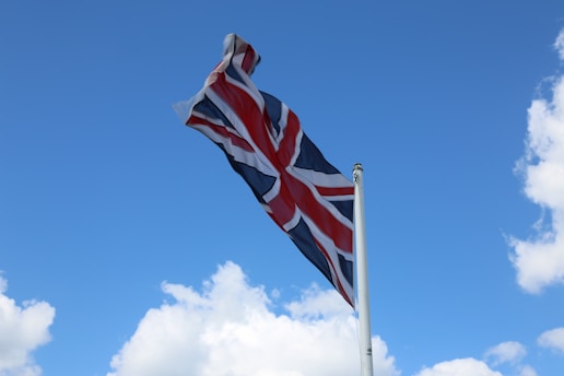 A Union Jack flag waves in the breeze against a bright blue sky with scattered white clouds.