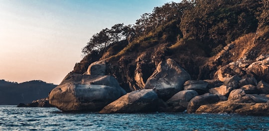 brown rocky mountain beside body of water during daytime in Goa India