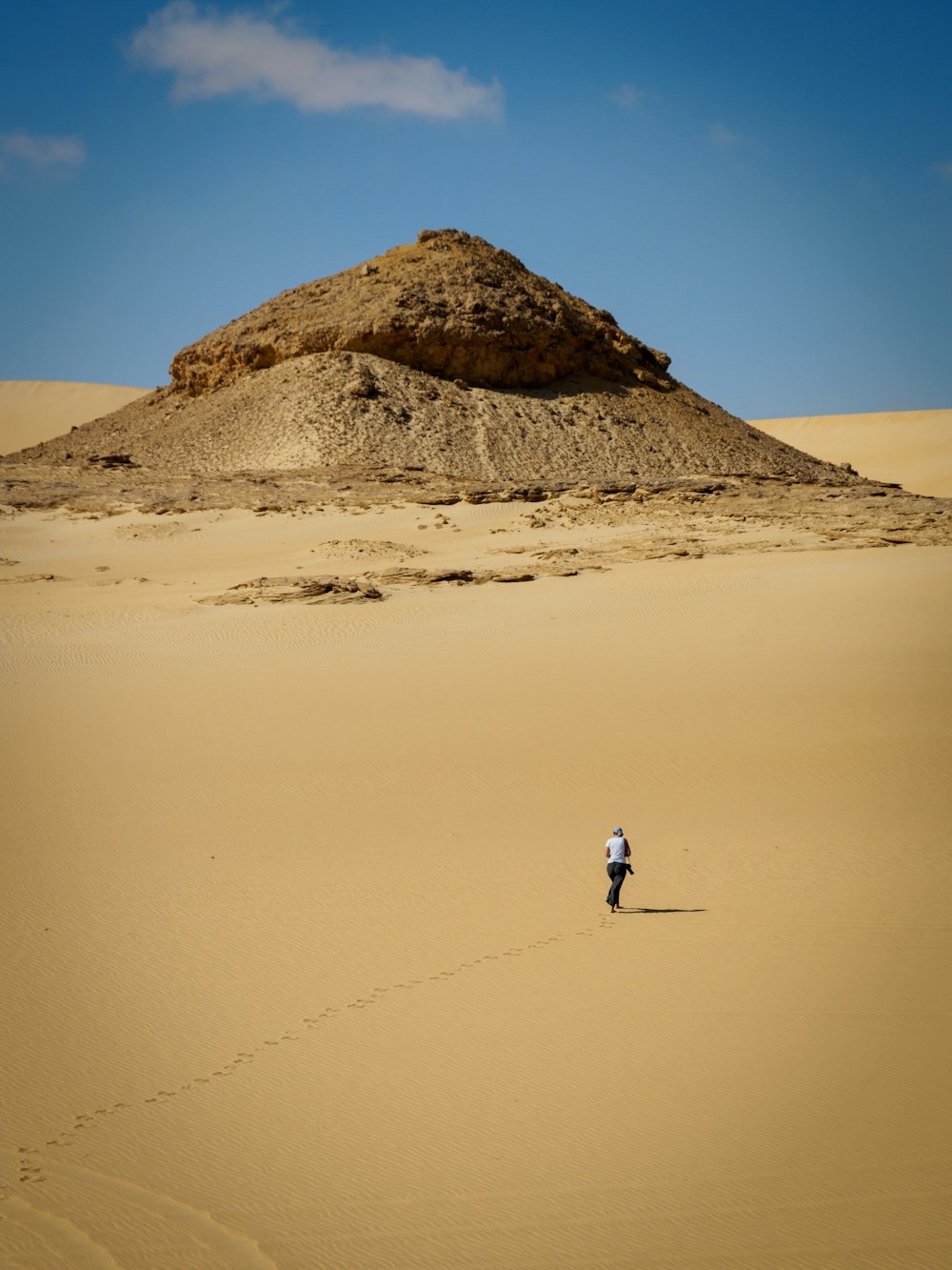 昼間、茶色の砂の上を歩く白いシャツの男