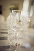 An elegant dining table setting with tall wine glasses and smaller glassware aligned in a row. The focus is on the glassware, creating a sophisticated and refined atmosphere.