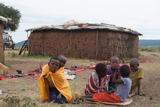 woman in red and white dress sitting on green grass field in Maasai Mara National Reserve Kenya